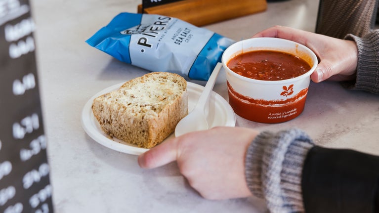 Someone is picking a takeaway soup, roll and packet of crisps from a kiosk counter